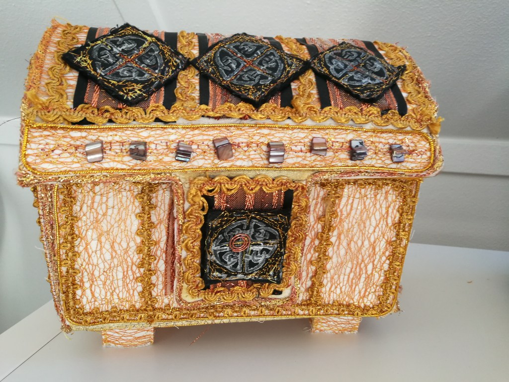 The primary subject is a decorative textile chest. It resembles a treasure chest in appearance, although it seems more stylized and less realistic.